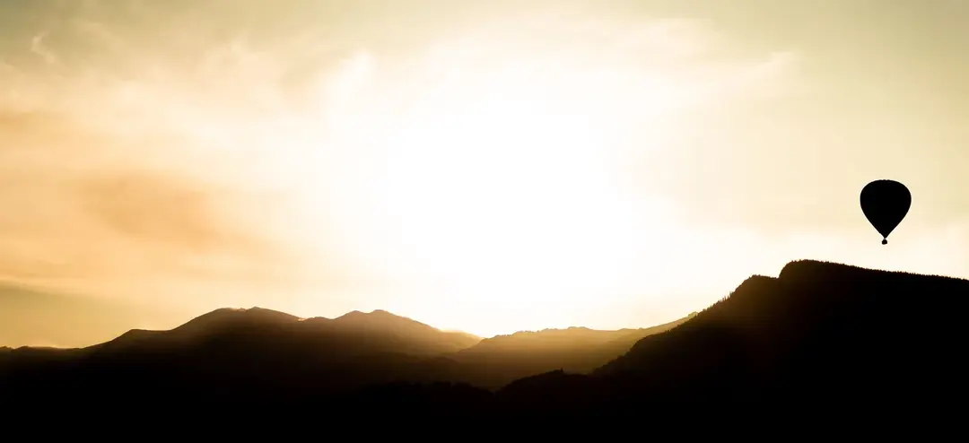 A hot air balloon silhouetted above mountains in golden light