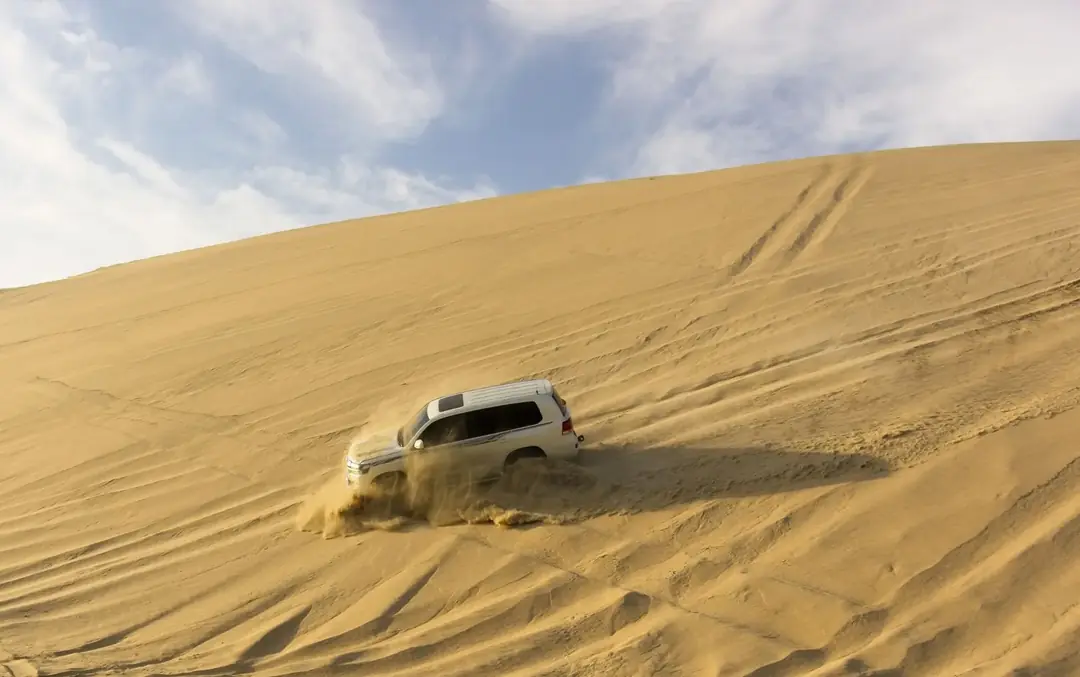 A 4x4 vehicle crossing golden sand dunes