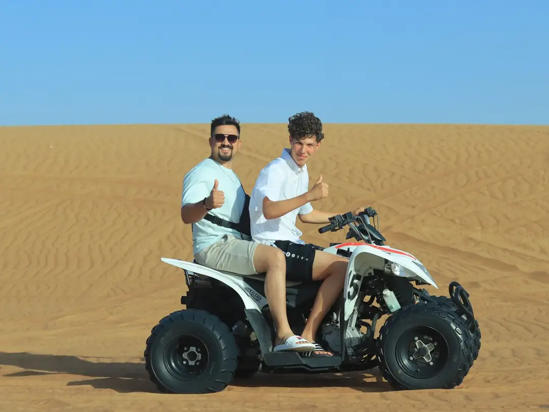 Two riders on a quad bike on golden sand dunes